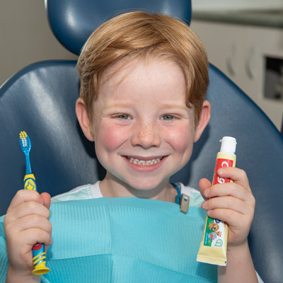 Child patient holding up a toothbrush and toothpaste at Maple Dental